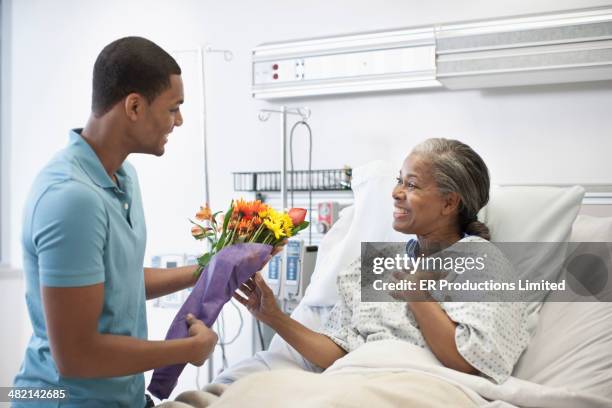 man bringing mother flowers in hospital - er visit stock pictures, royalty-free photos & images