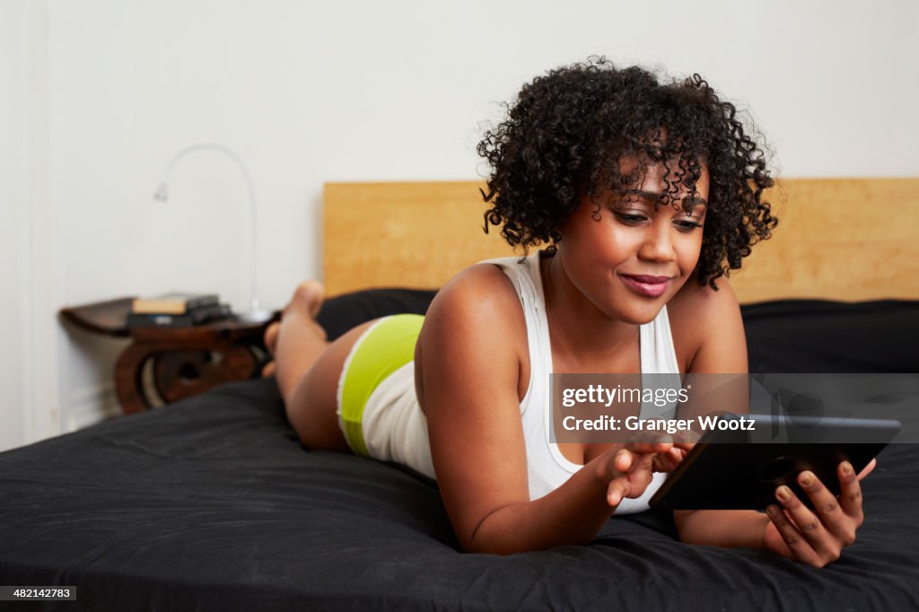 Mixed race woman using digital tablet on bed