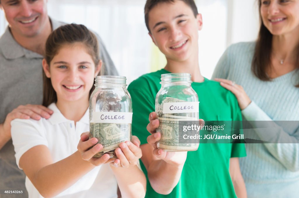 Proud Caucasian parents watching children with college savings jars