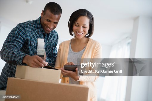 Couple with digital tablet taping up moving boxes Couple with digital tablet taping up moving boxes