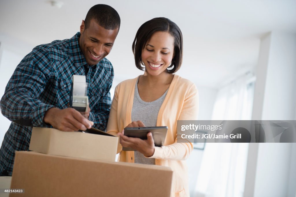 Couple with digital tablet taping up moving boxes