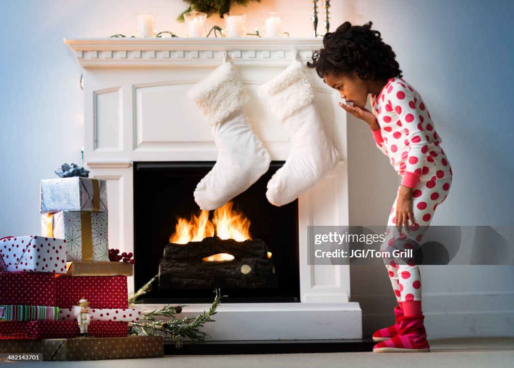 Surprised Black girl in pajamas looking down at Christmas gifts