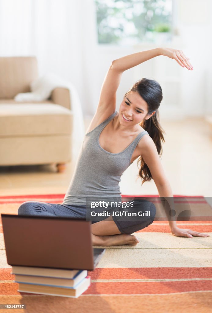 Hispanic woman on rug stretching in front of laptop