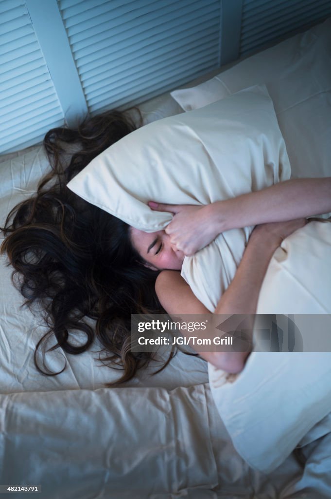 Frustrated Hispanic woman gripping pillow in bed