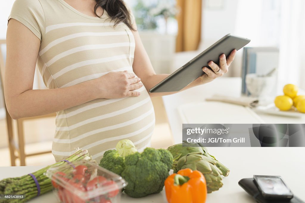 Pregnant Japanese woman using digital tablet in kitchen