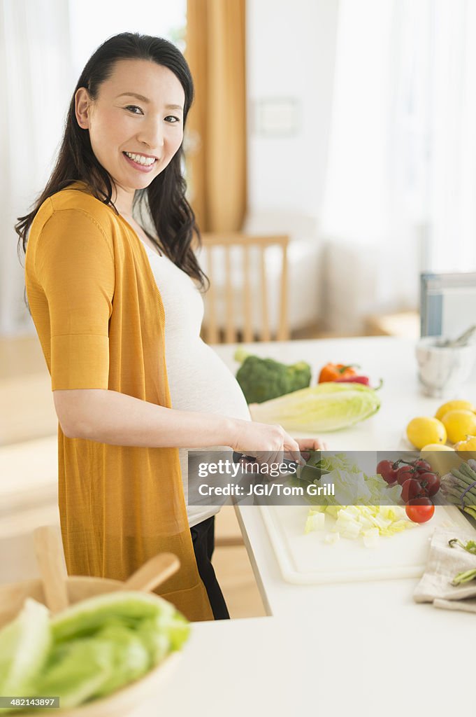 Portrait of pregnant Japanese woman slicing vegetables in kitchen