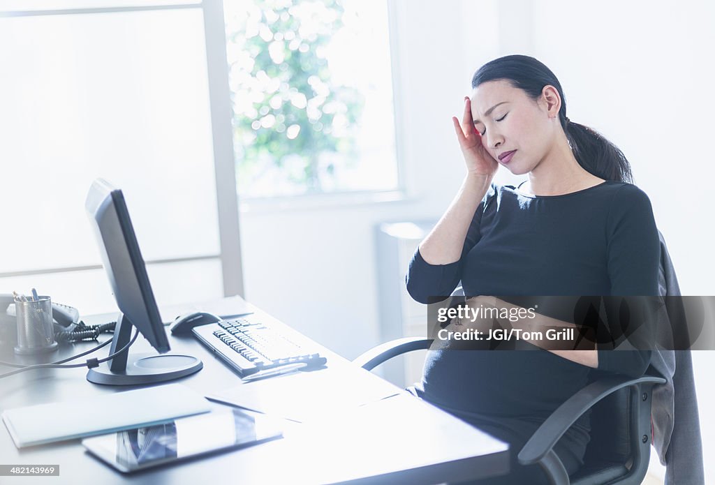 Tired pregnant Japanese businesswoman at desk