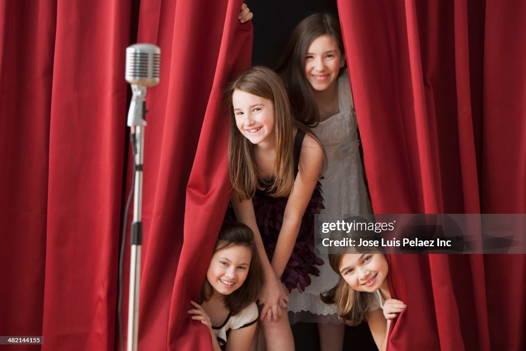 Portrait of Caucasian girls peering from behind stage curtain