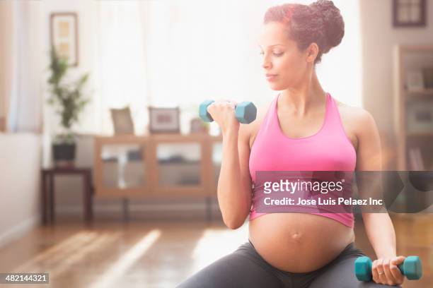 pregnant mixed race woman exercising with dumbbells - prenatal care stock pictures, royalty-free photos & images
