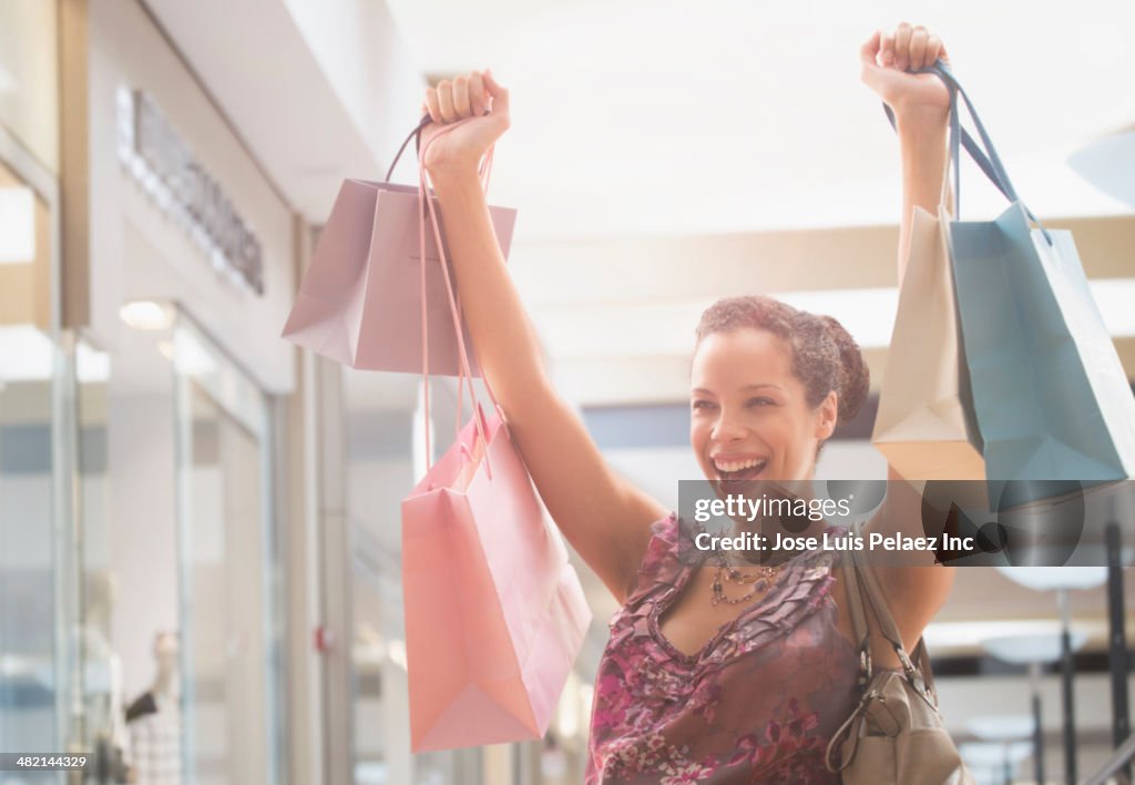 Pregnant mixed race woman cheering with shopping bags