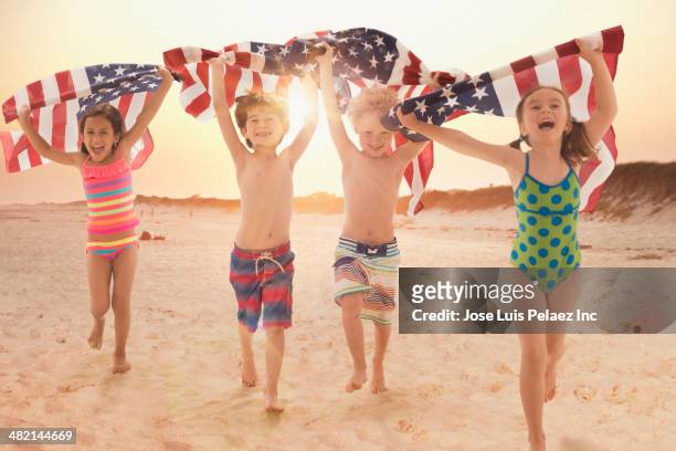 enthusiastic children carrying american flags on beach - american flag beach stock pictures, royalty-free photos & images
