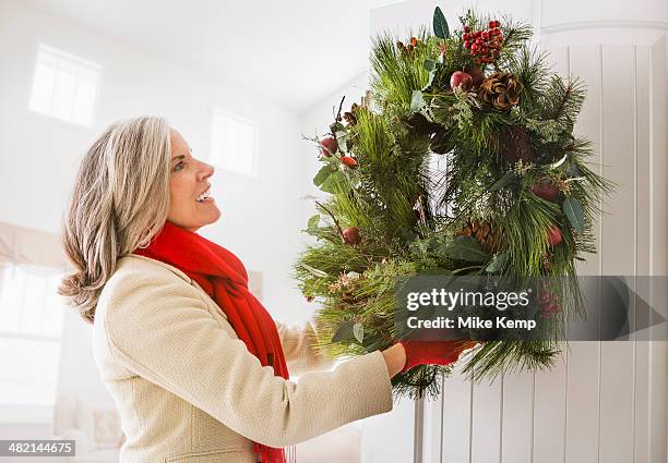 caucasian woman hanging christmas wreath on door - draped scarf stock pictures, royalty-free photos & images