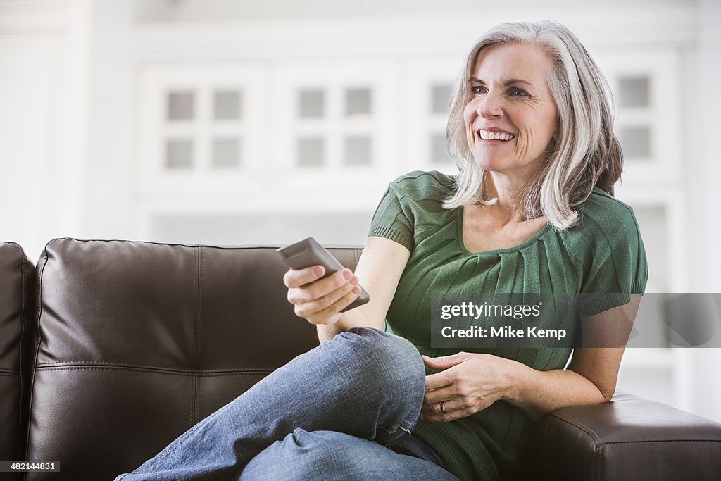 Happy Caucasian woman watching TV on sofa