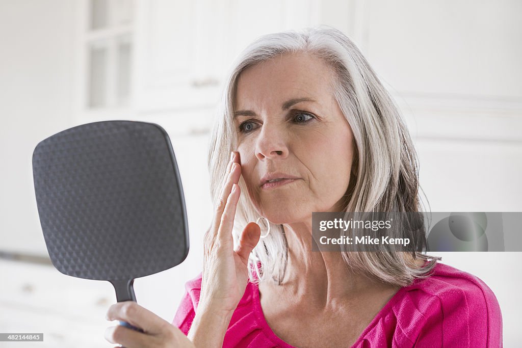 Caucasian woman looking at skin in mirror
