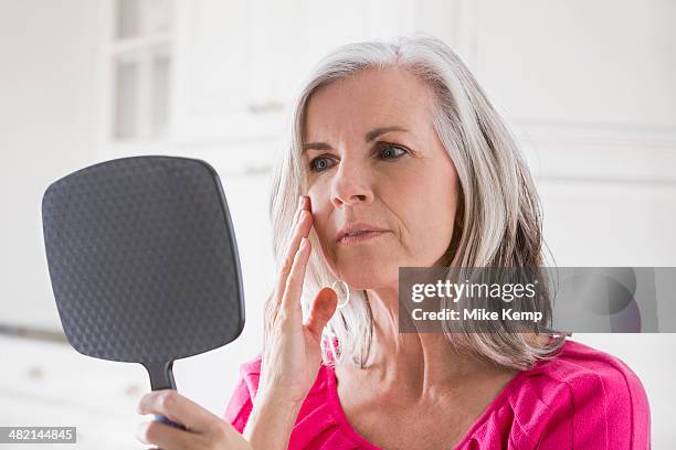 caucasian woman looking at skin in mirror - mature women skincare stock pictures, royalty-free photos & images