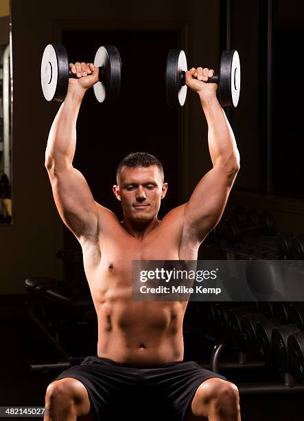 caucasian man with bare chest lifting dumbbells overhead - schulterpresse stock-fotos und bilder