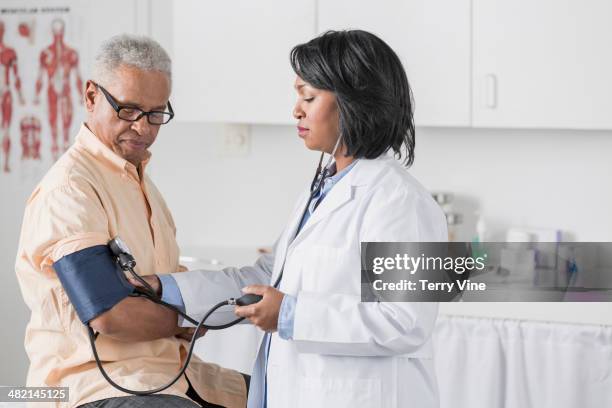 african american doctor checking senior man's blood pressure - blood pressure gauge stock pictures, royalty-free photos & images