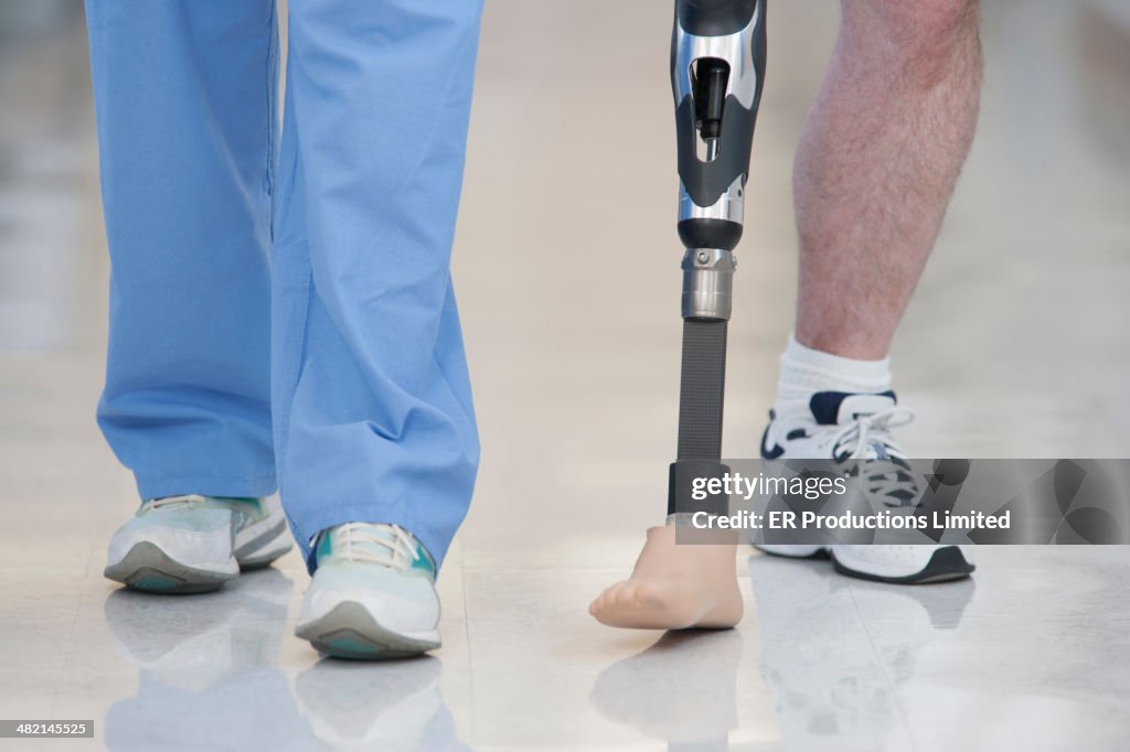 Nurse helping man walk with prosthetic leg
