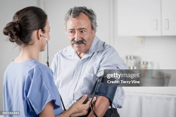 nurse checking senior man's blood pressure - hispanic medical exam stock pictures, royalty-free photos & images