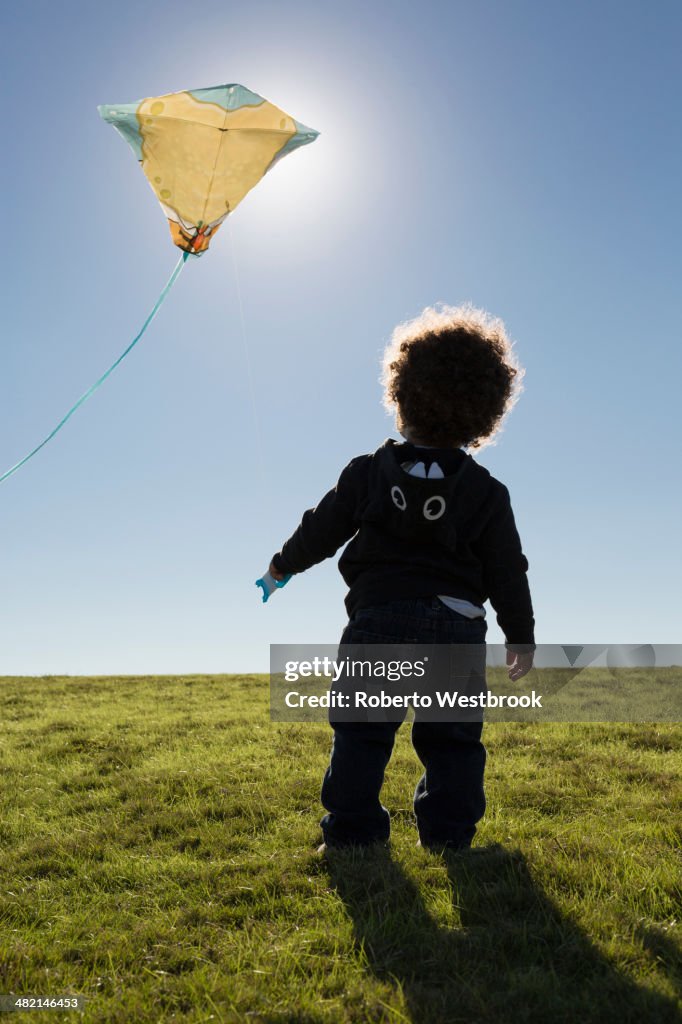 Mixed race boy watching kite flying against blue sky