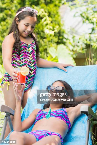 mixed race girl serving sister juice at poolside - diva stock-fotos und bilder