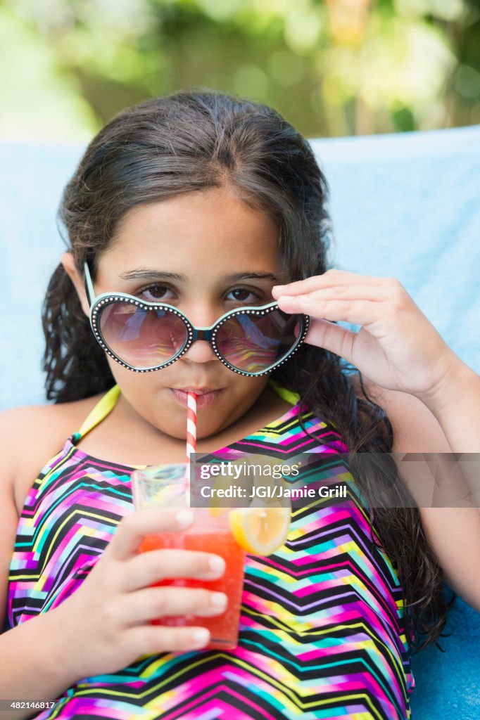 Mixed race girl sipping juice at poolside