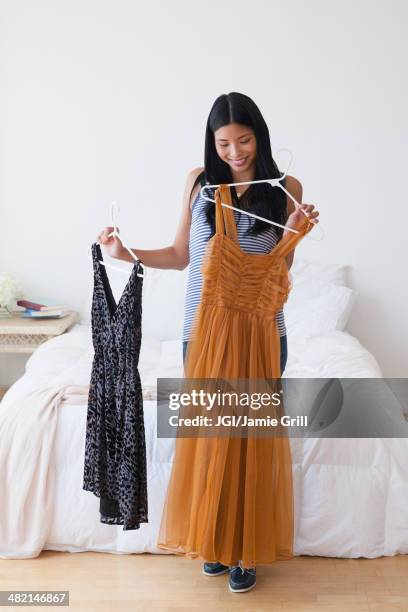 chinese woman picking out dresses in bedroom - holding two things foto e immagini stock