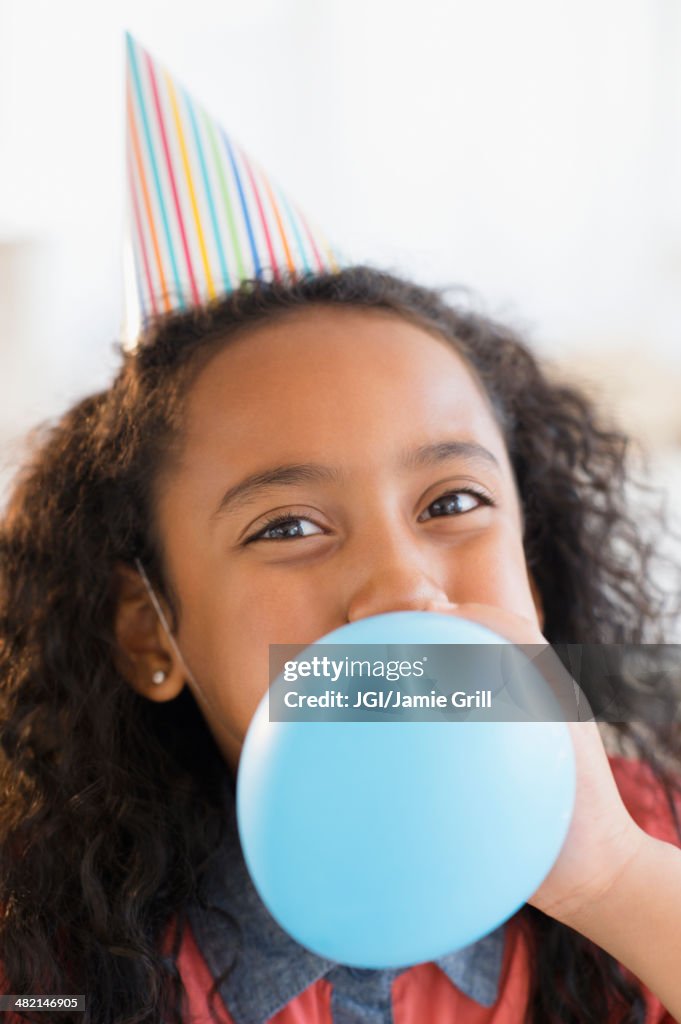 Mixed race girl inflating balloon at birthday party