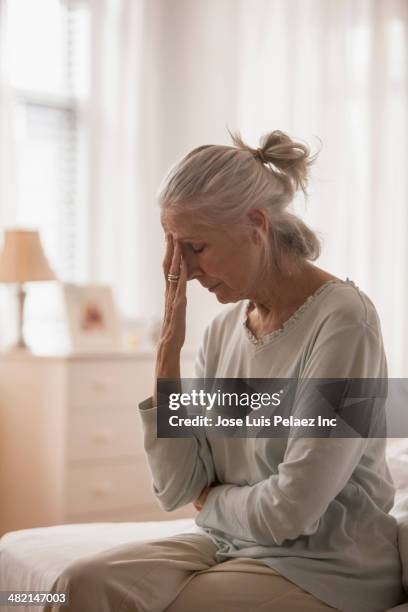 senior caucasian woman rubbing her forehead on bed - woman hand crossed stock-fotos und bilder