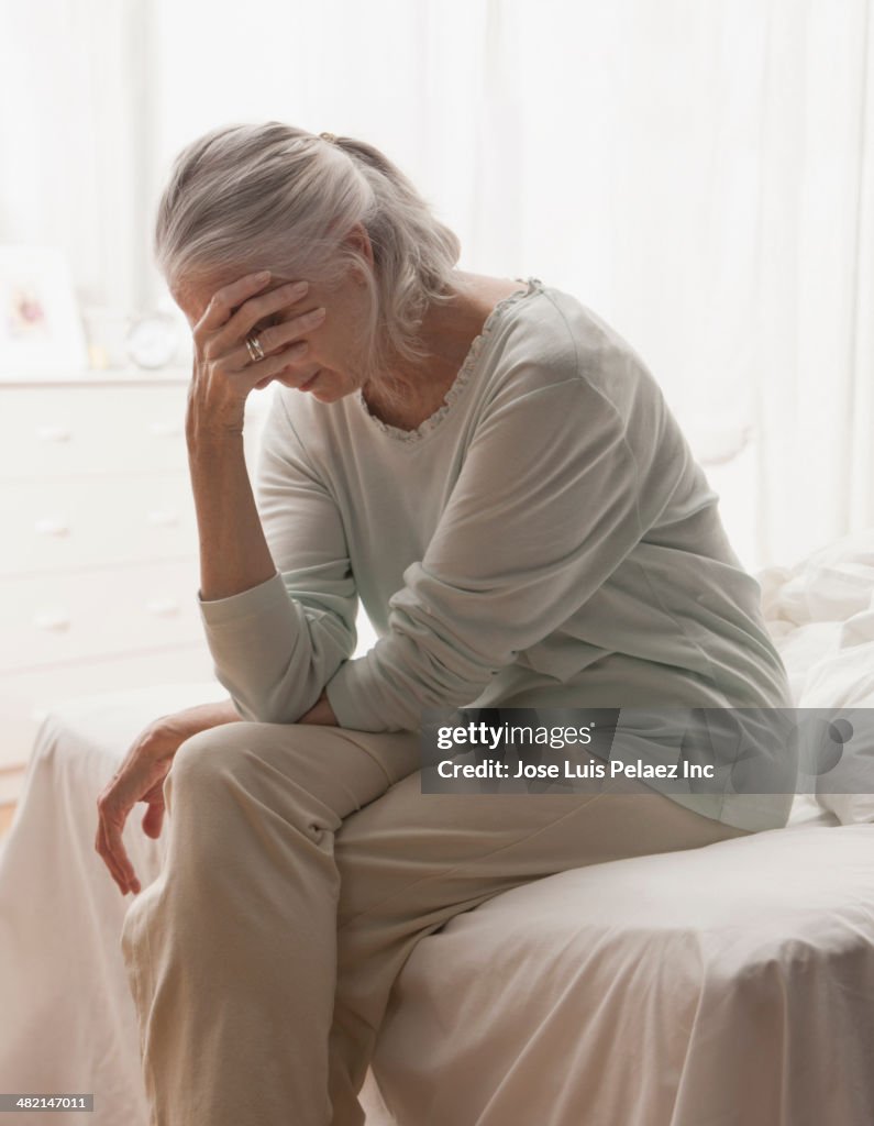 Senior Caucasian woman holding head in hand on bed