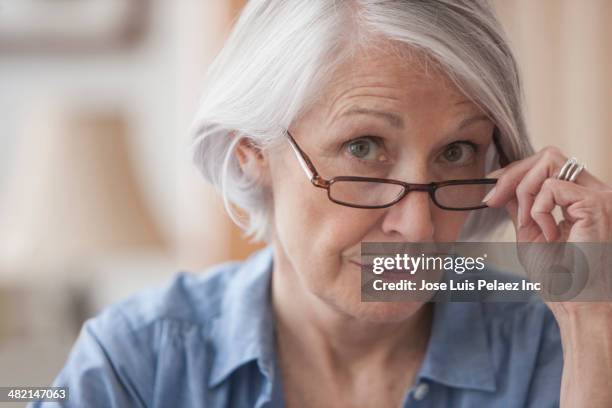 senior caucasian woman peering over her eyeglasses - suspicion 個照片及圖片檔