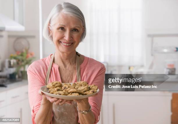 senior caucasian woman holding plate of cookies - woman baking stock-fotos und bilder