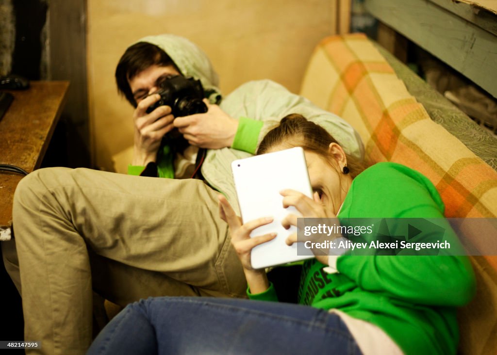 Caucasian man photographing girlfriend on sofa