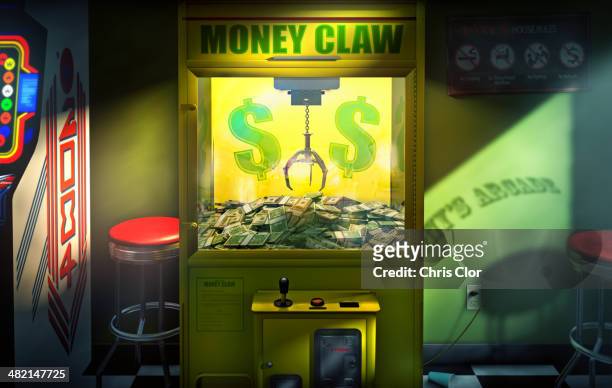 claw grabbing money in money claw arcade machine - arcade machine stockfoto's en -beelden