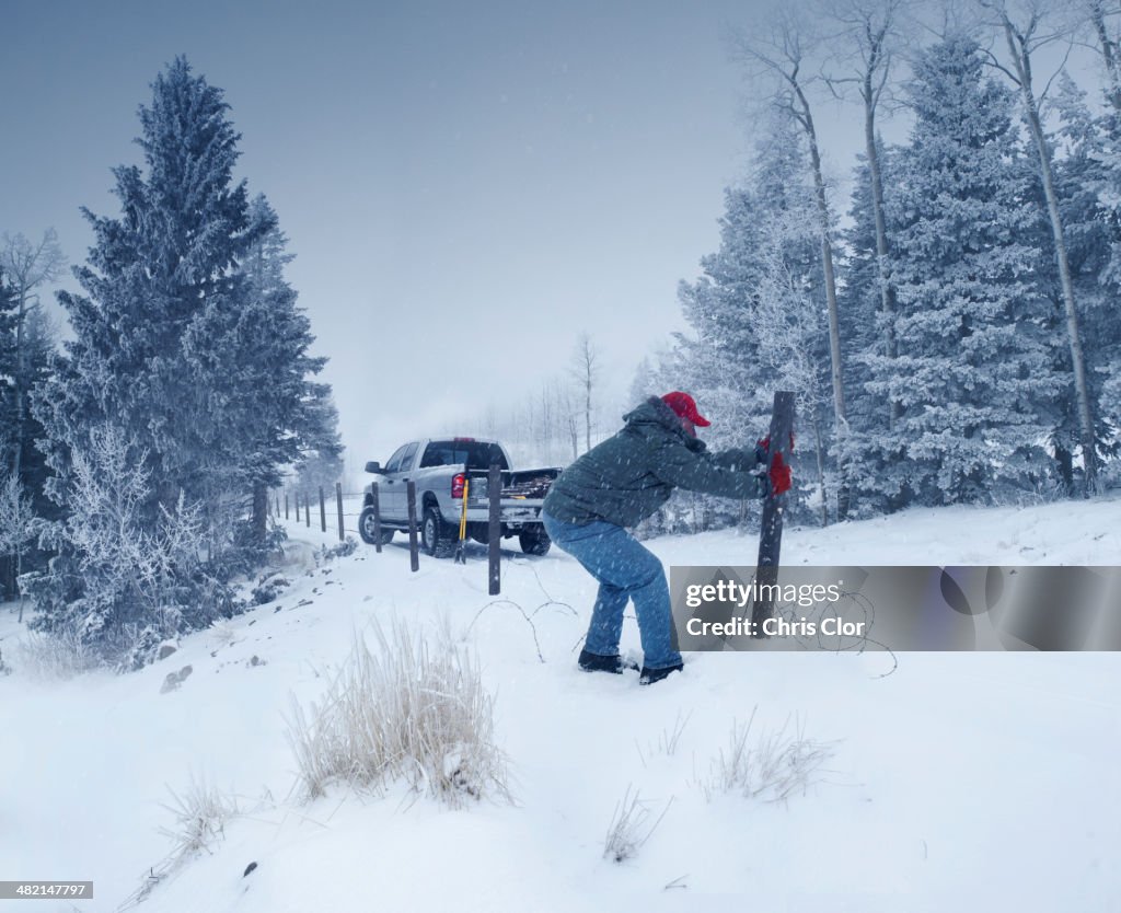 Man repairing wooden post in snowy ground