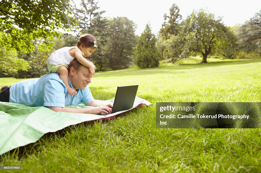 Father and baby girl using laptop in park