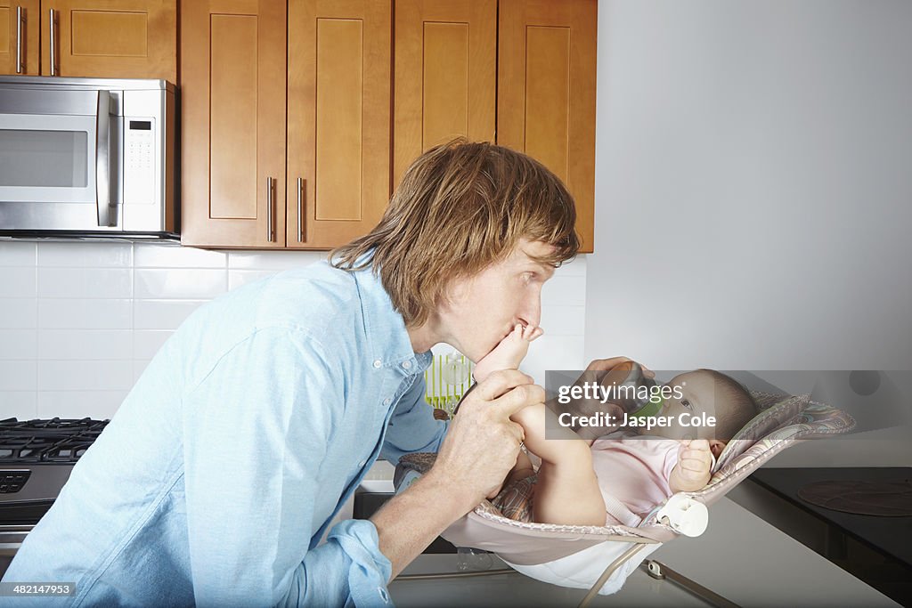 Father kissing baby's feet in chair