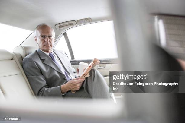 caucasian businessman reading newspaper in car - newspaper luxury stock-fotos und bilder
