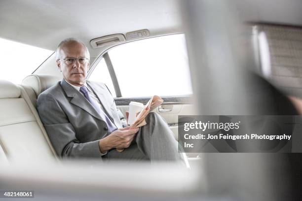 caucasian businessman reading newspaper in car - newspaper luxury stockfoto's en -beelden