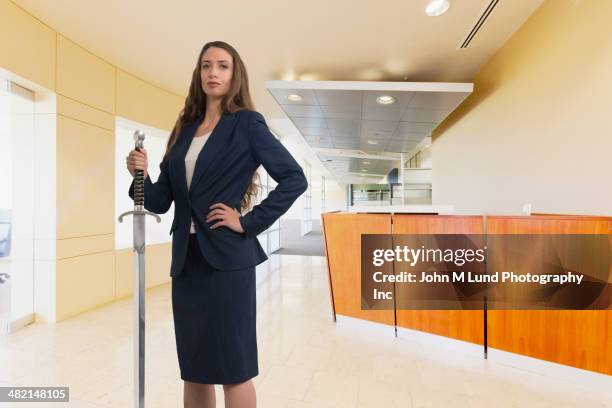 caucasian businesswoman holding sword in office - holding sword stock pictures, royalty-free photos & images