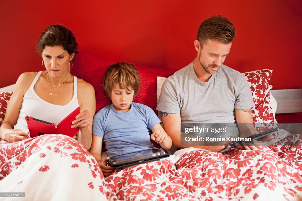 Caucasian family using digital tablets in bed