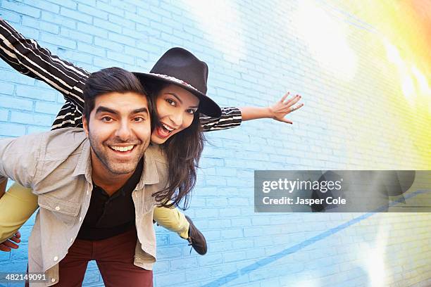 indian couple piggybacking along brick wall - couple celebrating stock pictures, royalty-free photos & images