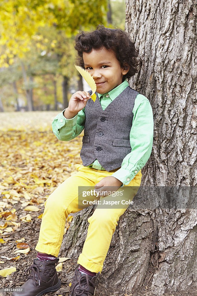 Mixed race boy holding leaf in park