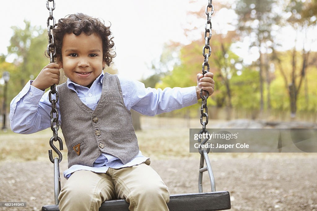 Mixed race boy sitting on swing in park