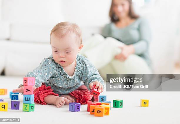 caucasian baby girl with down syndrome playing with blocks - down syndrome baby stock pictures, royalty-free photos & images