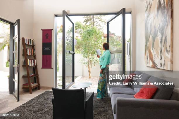 hispanic woman standing at glass doors - french doors stockfoto's en -beelden