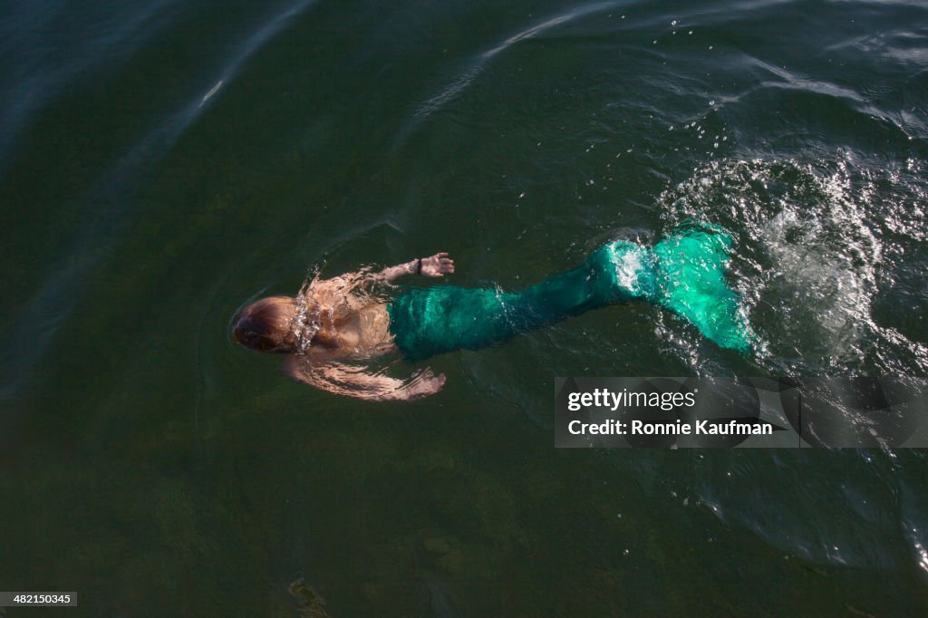 Caucasian woman swimming in mermaid costume in still lake