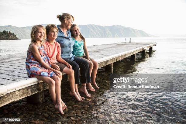 mother and children sitting on wooden dock in still lake - woman pier stock pictures, royalty-free photos & images