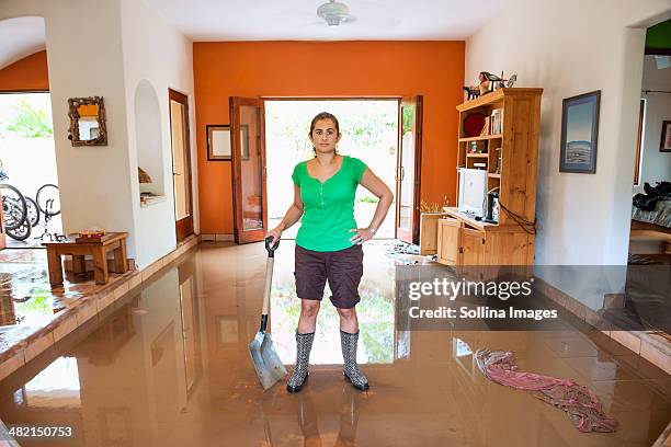 hispanic woman shoveling water out of flooded house - flooded home stock pictures, royalty-free photos & images