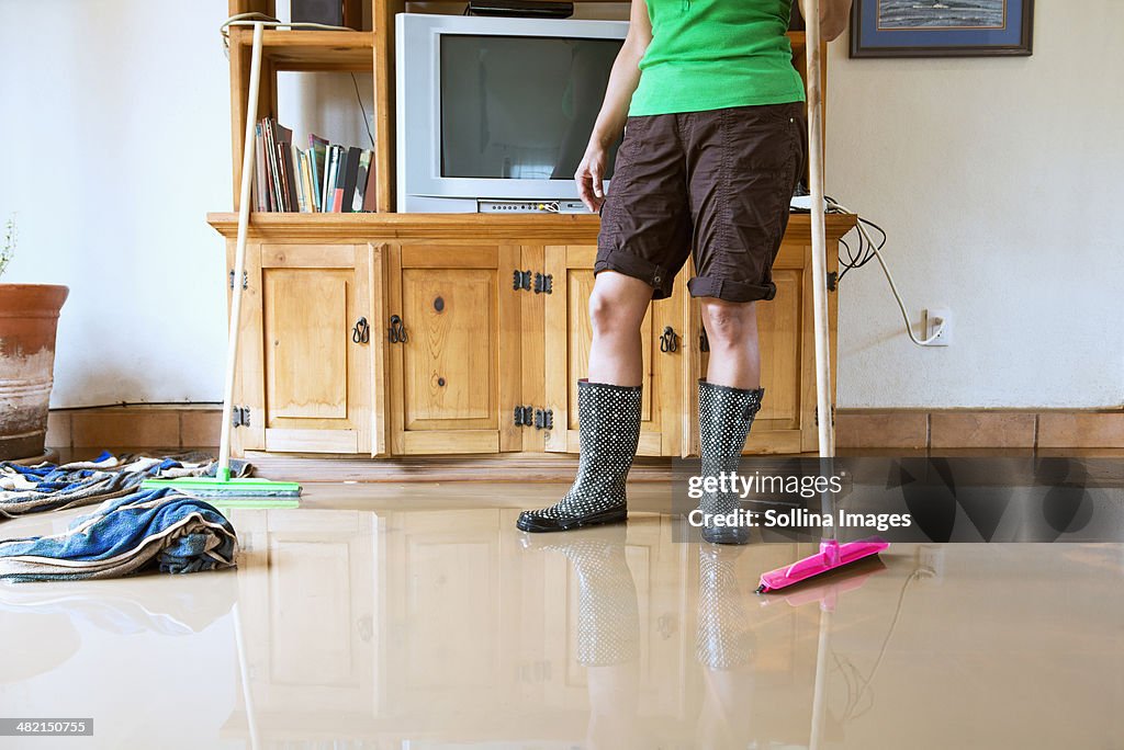 Hispanic woman sweeping water out of flooded house